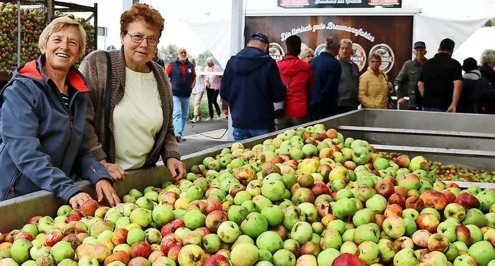 Zwei Frauen lachen neben einer Wanne voller frisch geernteter Äpfel beim Apfelfest