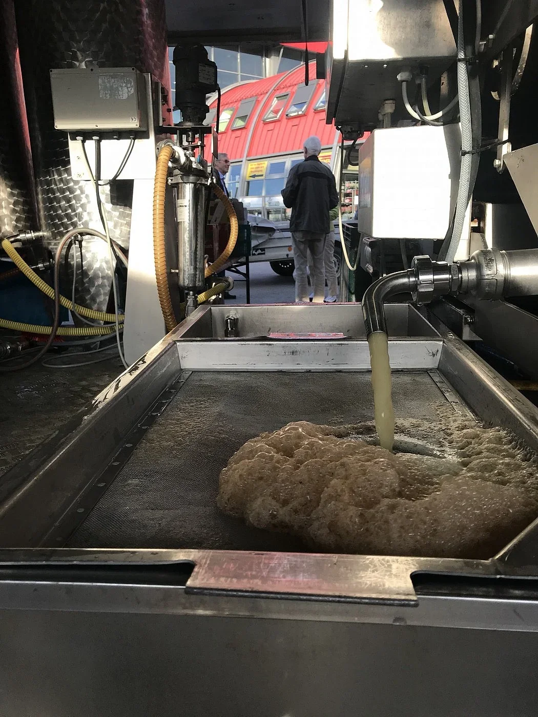 Saft läuft aus der mobilen Presse, im Hintergrund Besucher am Anhänger
