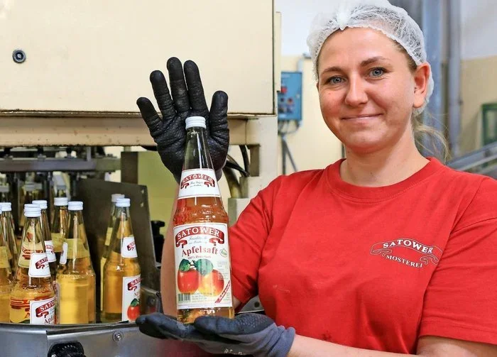 Mitarbeiterin hält eine Flasche Apfelsaft an der Abfüllanlage
