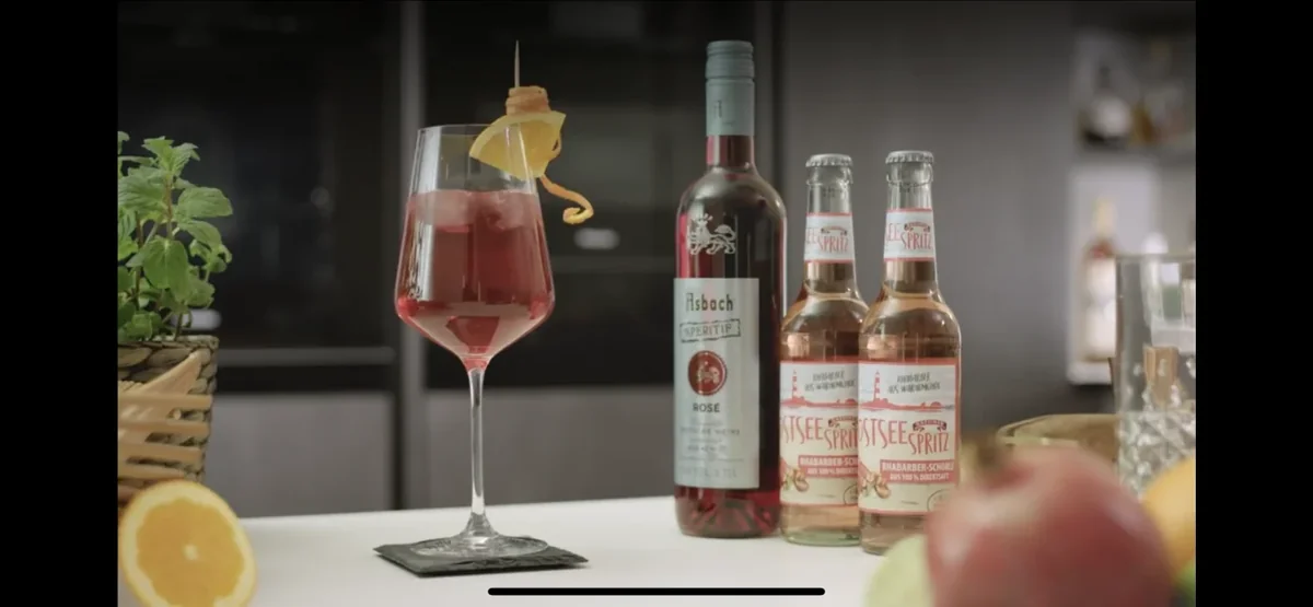 Glas Ostseespritz mit Rhabarbersaft-Flaschen und Zutaten auf der Theke