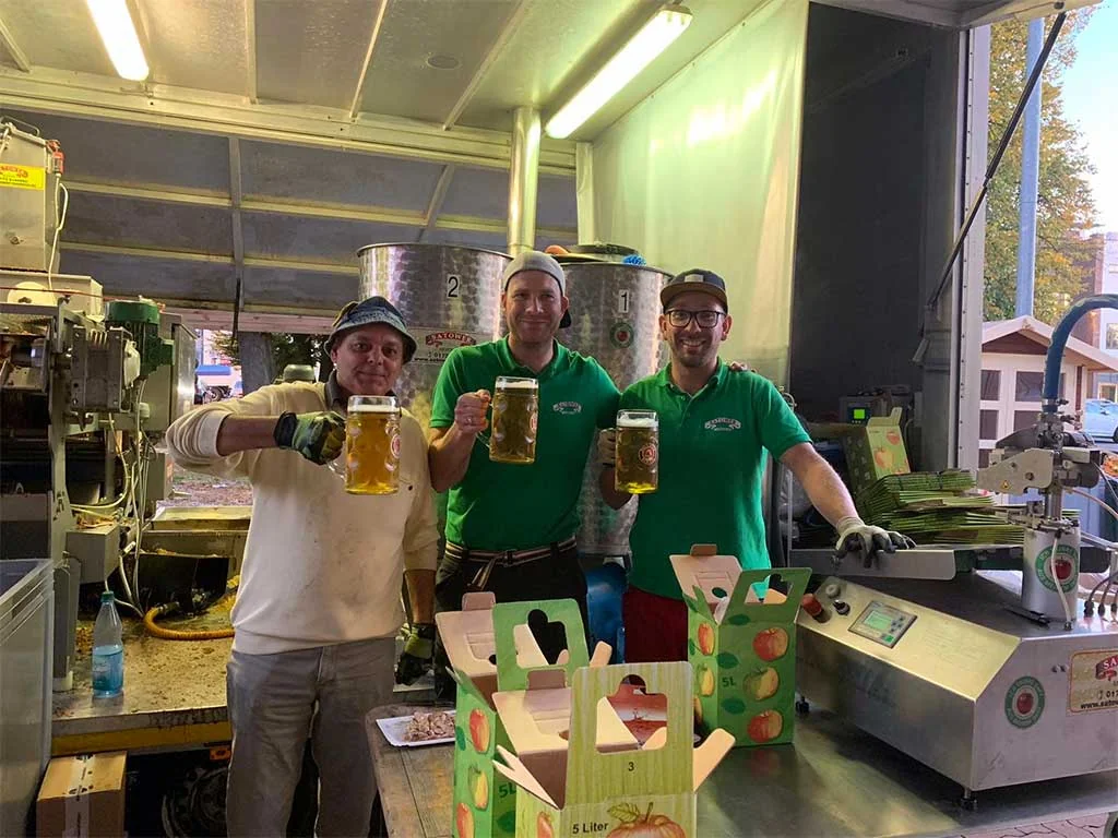 Drei Mitarbeiter mit Bierkrügen in der mobilen Saftpresse