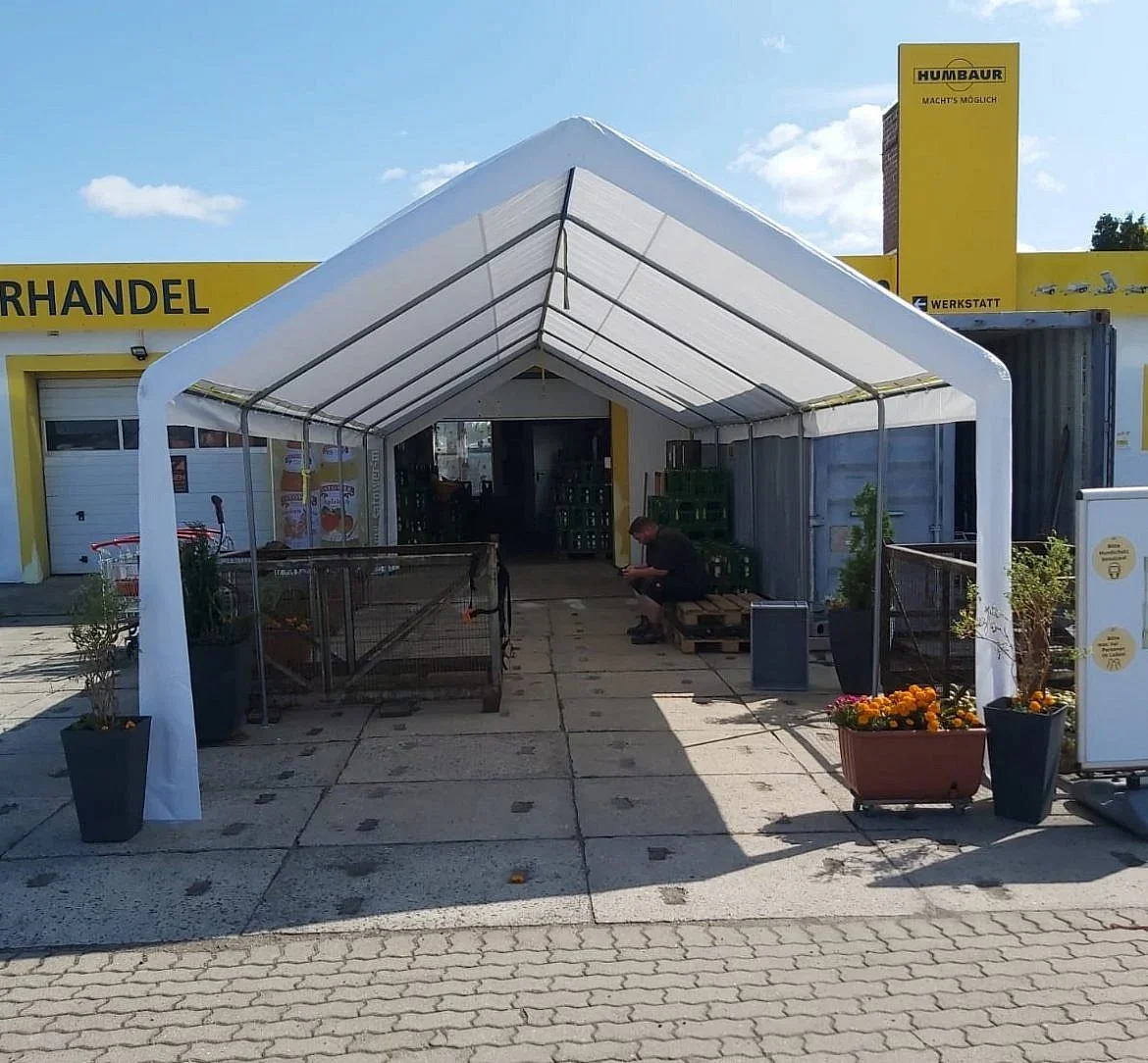 Weißes Verkaufszelt vor einem Autohandel mit gestapelten Getränkekisten